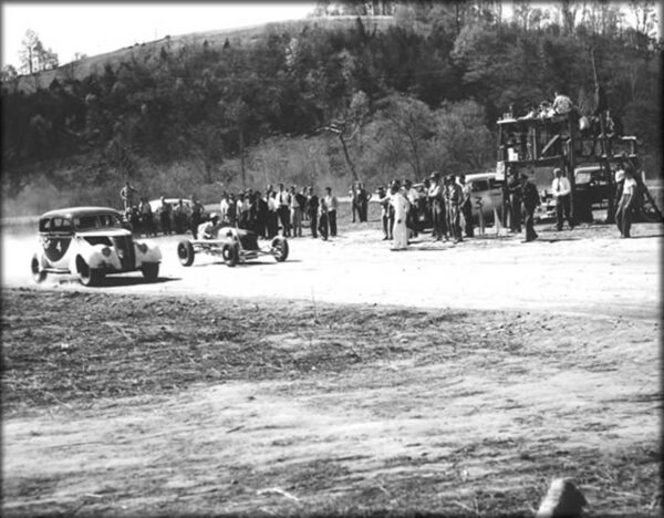 An old photo of old racing cars on a dirt road.