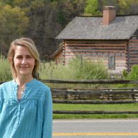 Bethany Worley standing outside with a road and a log cabin behind her.