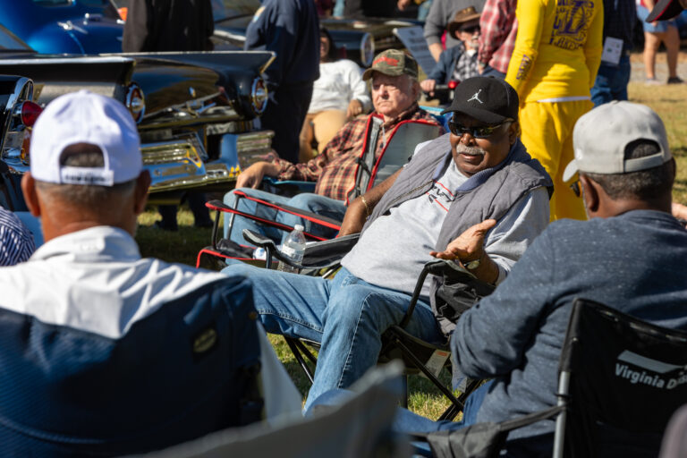 A group of men seated in folding chairs talking.