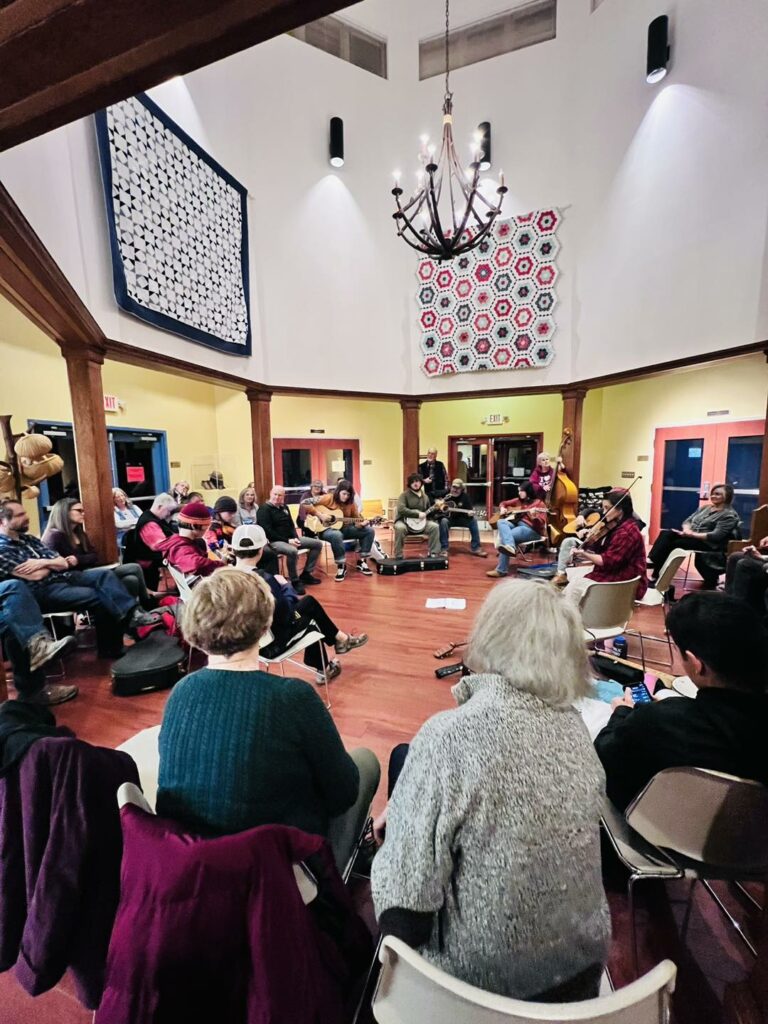 People seated in a large room listening to a group play music.