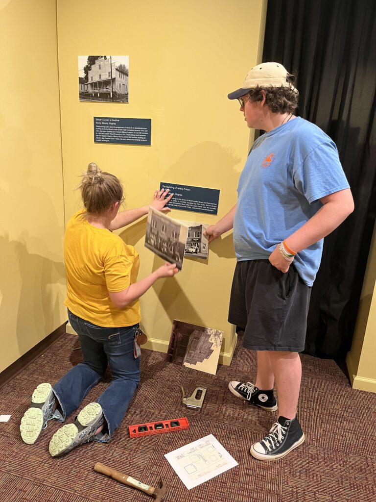 A woman and a man placing prints and photos on a wall.